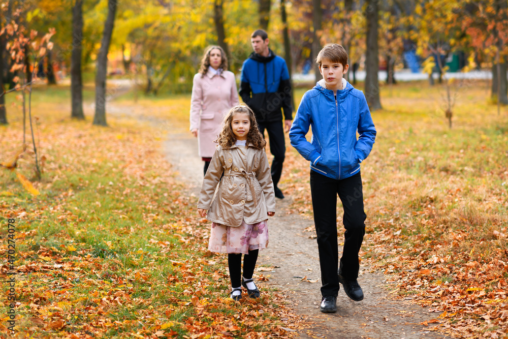 Family walks in the autumn park along the path. A beautiful nature and trees with yellow leaves. Bright sunlight.