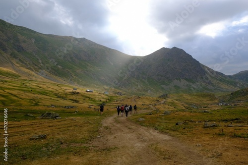 Beautiful mountain view with silhouettes of hiking tourists walking through green valley on rainy day. They have backpacks with colorful rain covers. Dobërdol, Albanian Alps, Peaks of Balkans © Iwona