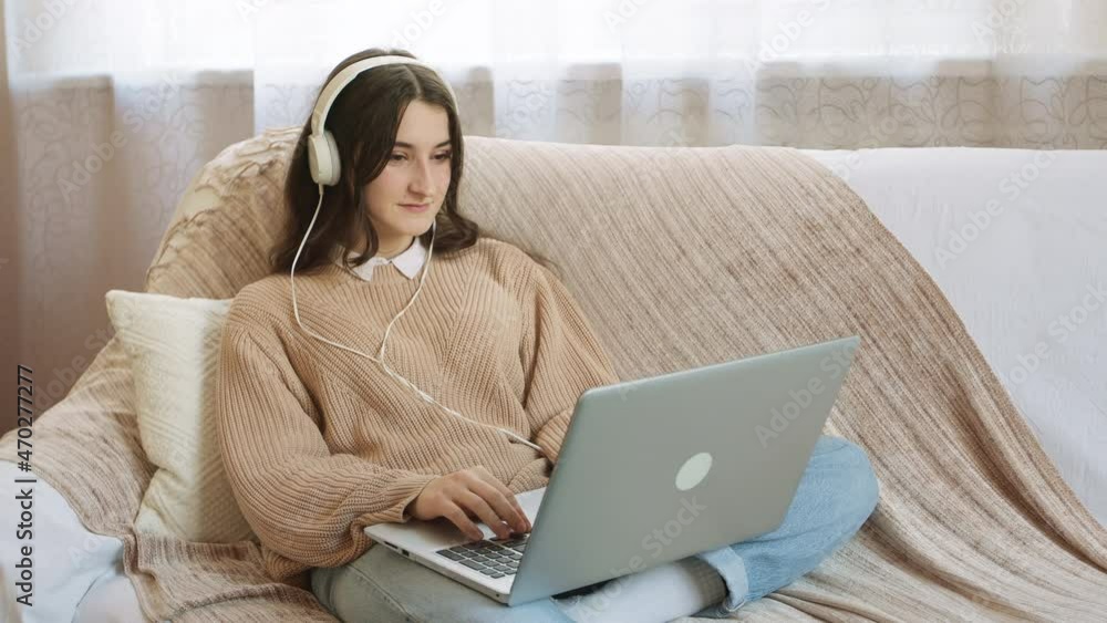 Young woman works remotely at home using a laptop. A student with headphones is watching an online educational webinar. Young woman works remotely at home using a laptop. A student with headphones is watching an online educational webinar.