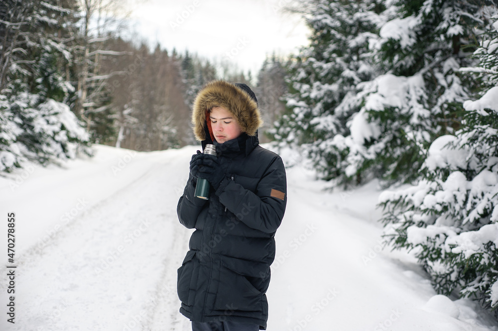 Teenage boy walks through a snowy forest on a cold winter day with a hot drink in a thermos. Healthy lifestyle. Useful activity. Teenage boy walks through a snowy forest on a cold winter day with a hot drink in a thermos. Healthy lifestyle. Useful activity.
