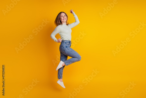 Photo of astonished funky sporty lady jump rejoice win wear green shirt jeans sneakers isolated on yellow background