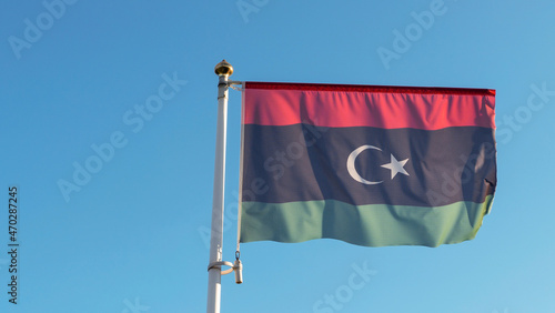 National flag of Islamic republic of Libya on a flagpole in front of blue sky with sun rays. Diplomacy concept.