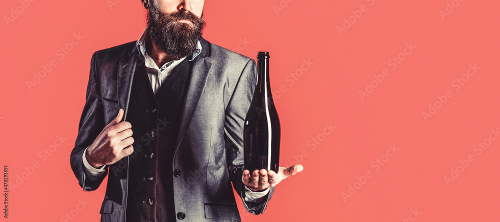 Naklejka premium The person holds a red wine bottle in a hand. Man holding bottle with champagne, wine. Bearded man with a bottle champagne of and glass