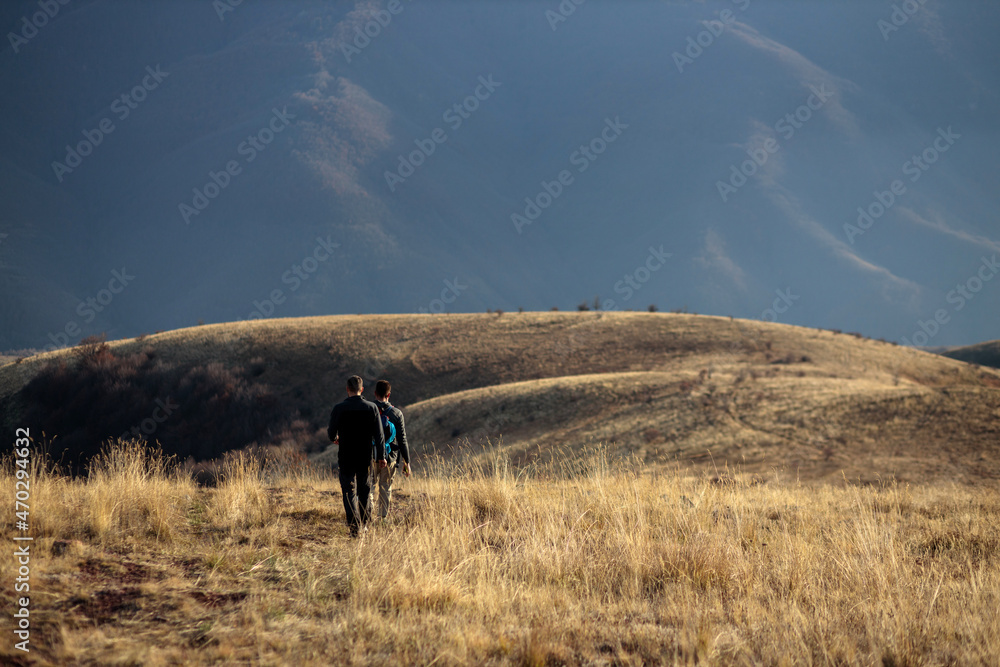 Two young men hiking and trekking over rolling meadows of Stara planina in late autumn afternoon sun
