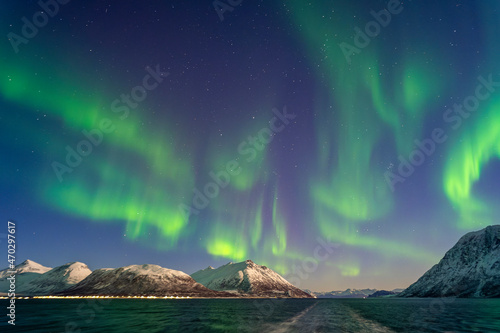 tanzende Nordlichter über Reinøya und Karlsøya. grün, gelb, pink Aurora Borealis im Ullsfjord, Troms, Norwegen. verschneite Berge auf den Inseln. sternenklarer Himmel über dem Postschiff.