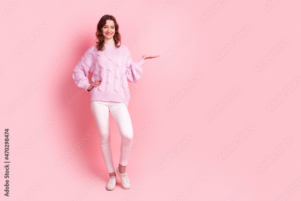 Full length photo of young cheerful woman hold hand promotion offer advertise isolated over pink color background Full length photo of young cheerful woman hold hand promotion offer advertise isolated over pink color background