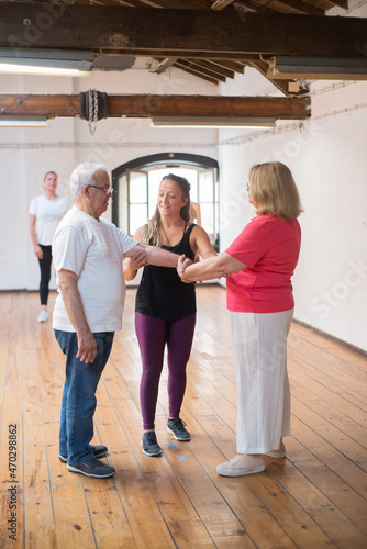 Young Caucasian instructor demonstrating dance moves to seniors. Positive female teacher in purple leggings showing patterns to retired partners in glasses. Dance, hobby, healthy lifestyle concept