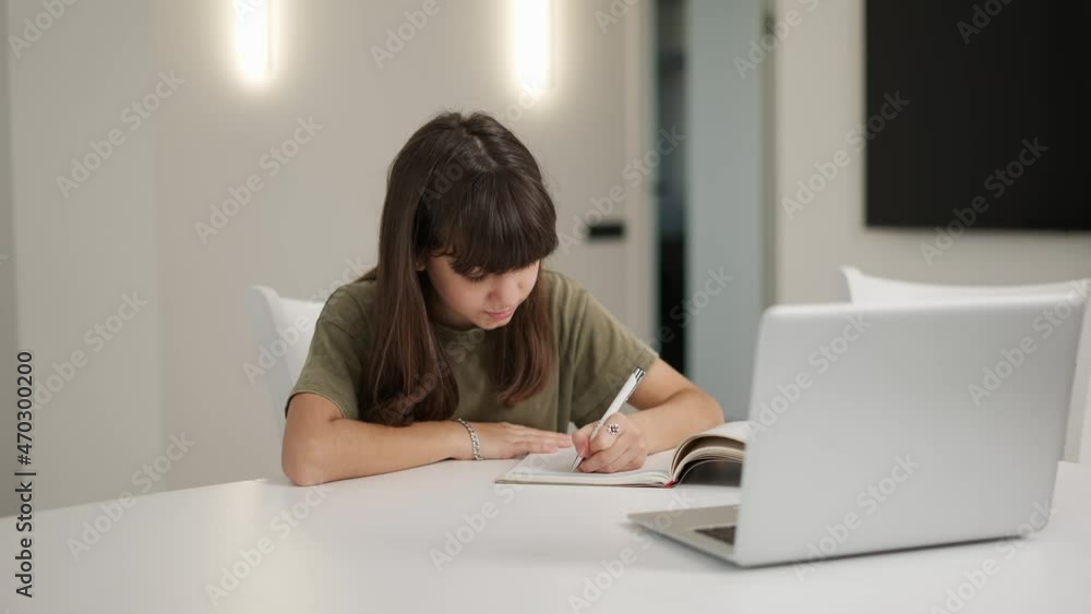 Brunette teen girl sitting at the desk doing her homework using a laptop Brunette teen girl sitting at the desk doing her homework using a laptop
