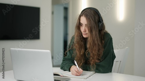 Concertrated student girl has distant lesson on laptop, making notes photo