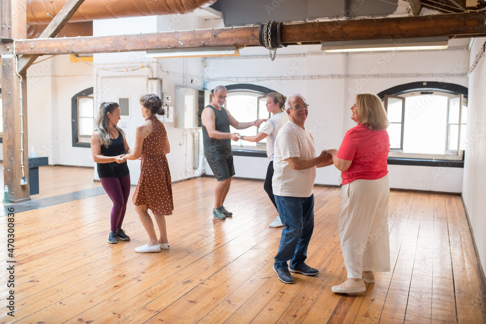 Cheerful old Caucasian couples dancing and laughing in studio. Retired partners having fun while learning dancing steps. Dance, hobby, healthy lifestyle concept Cheerful old Caucasian couples dancing and laughing in studio. Retired partners having fun while learning dancing steps. Dance, hobby, healthy lifestyle concept