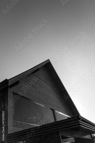 Black and white minimalist photograph of house roof and plane in sky. © rafaelcampezato
