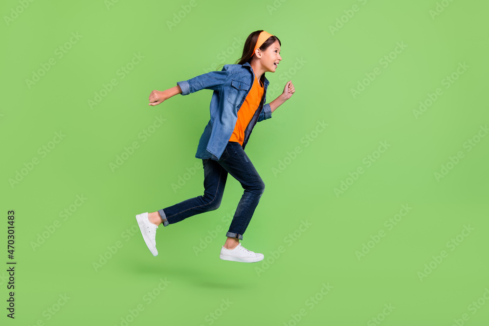 Photo of funny charming student girl wear denim shirt smiling jumping high running fast isolated green color background Photo of funny charming student girl wear denim shirt smiling jumping high running fast isolated green color background