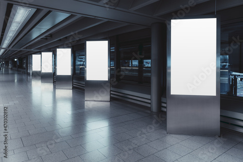 Five empty vertical posters mock-ups glowing with a LED neon light in an airport terminal; a group of blank banners templates in a corridor of a shopping mall; mockups of 5 indoor billboards in a hall