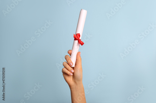 Student holding rolled diploma with red ribbon on light blue background, closeup