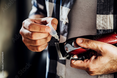 Foto Barber putting oil in his hair trimmer machine with a little bottle