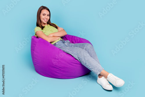 Full size photo of funny brunette millennial lady sit on bag crossed arms wear t-shirt jeans shoes isolated on blue color background