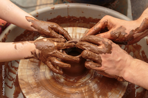 The child moulds from clay a pot on a potter's wheel. Adults help the child to work with clay.