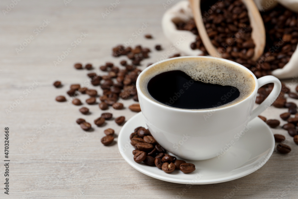 Cup of aromatic coffee and beans on light wooden table. Space for text Cup of aromatic coffee and beans on light wooden table. Space for text
