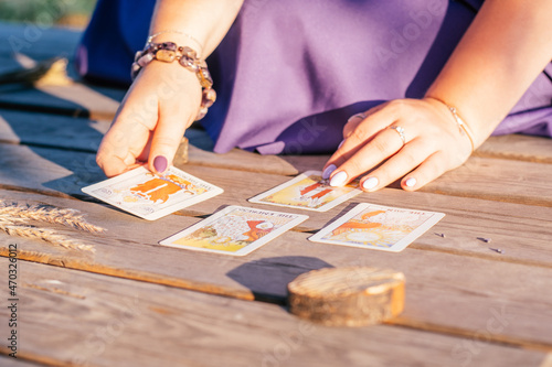 Woman's hand with purple nails lays one of four Tarot cards spread out on wooden surface next to spikelets and lavender