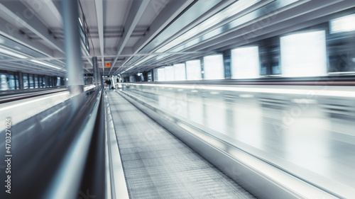 A long airport travelator in an airport with a strong motion blur and shallow depth of field; a long-exposure shot of a modern moving walkway in a shopping mall with selective focus on a railing part