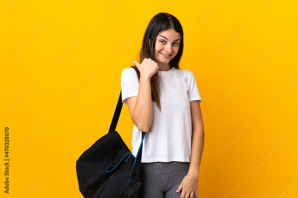 Young sport woman with sport bag isolated on yellow background pointing to the side to present a product Young sport woman with sport bag isolated on yellow background pointing to the side to present a product