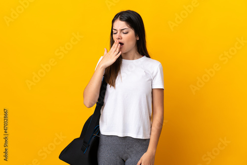 Young sport woman with sport bag isolated on yellow background yawning and covering wide open mouth with hand