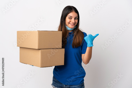 Young delivery woman protecting from the coronavirus with a mask isolated on white background pointing to the side to present a product