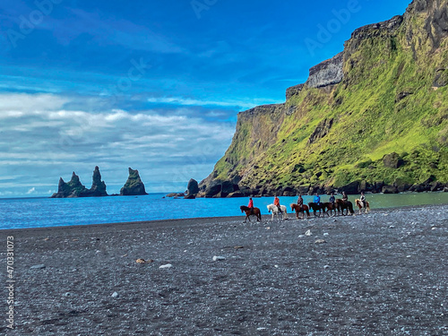 view to the beach with dark sand, horeses riding and impressive rock formation of the Reynisfjara, Iceland