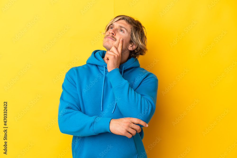 Handsome blonde man isolated on yellow background having doubts while looking up Handsome blonde man isolated on yellow background having doubts while looking up