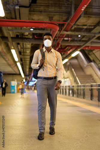 Man traveling and waiting at train station during covid and wearing face mask while social distancing and walking