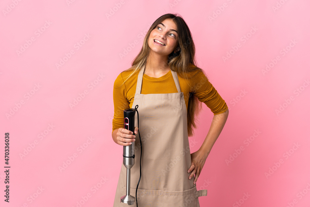 Young chef woman using hand blender isolated on pink background thinking an idea while looking up