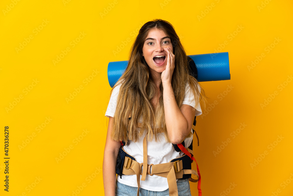 Young mountaineer woman with a big backpack isolated on yellow background shouting with mouth wide open Young mountaineer woman with a big backpack isolated on yellow background shouting with mouth wide open