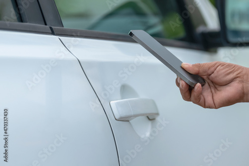 Hand of woman holding the smartphone near the car door.