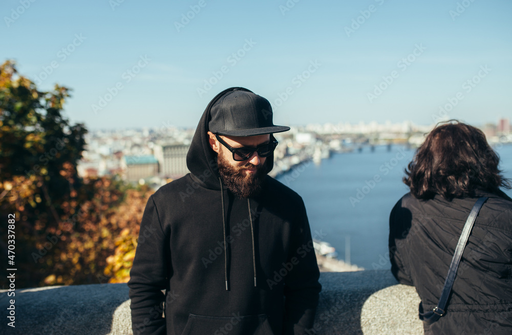 City portrait of handsome hipster guy wearing black blank hoodie with space for your logo or design. Mockup for print City portrait of handsome hipster guy wearing black blank hoodie with space for your logo or design. Mockup for print