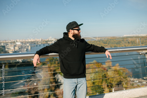 City portrait of handsome hipster guy wearing black blank hoodie with space for your logo or design. Mockup for print