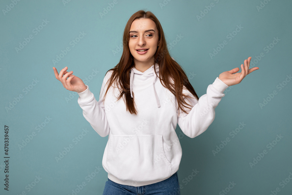 Photo of young positive happy beautiful brunette woman with sincere emotions wearing white hoodie isolated over blue background with copy space and shruging with hands Photo of young positive happy beautiful brunette woman with sincere emotions wearing white hoodie isolated over blue background with copy space and shruging with hands