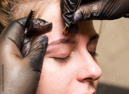 the master of permanent make-up prepares the client's eyebrows for the procedure, pulling hairs close-up with tweezers