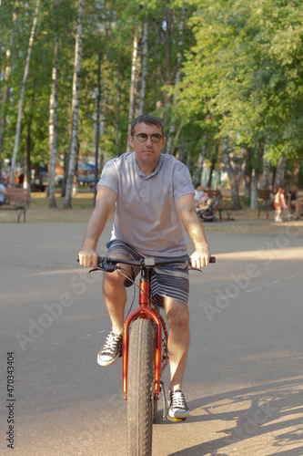 A man in dark glasses rides a bicycle in a public park in the summer. Sports and leisure © Alexander