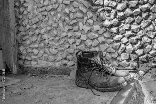 old dirty worn men's military motorcycle boots stand on the doorstep of the house. monochrome, black and white photo
