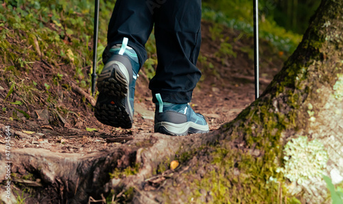 Close-up of women's hiking boots, walking with hiking poles on a mountain trail.