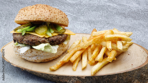 Close-up of tasty hot cheeseburger with cheddar cheese, hot chili pepper, french fries, american salad and cucumber pickle on a natural wooden tray