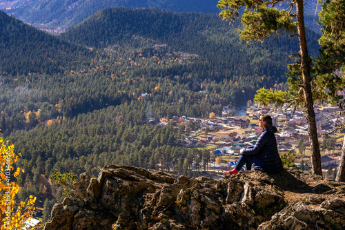 A girl on the edge of a cliff against the backdrop of mountains and the city. 
