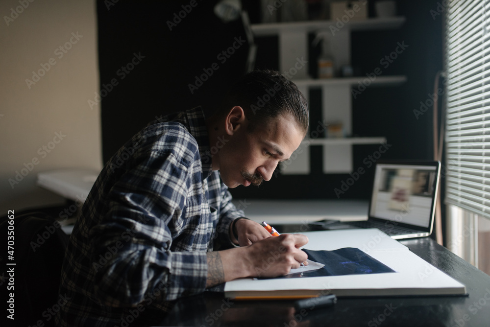 Male artist drawing in sketchbook at desk in artists studio Male artist drawing in sketchbook at desk in artists studio