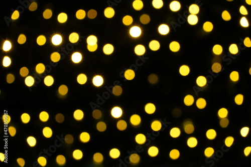 Defocuses Christmas lights in yellow shades on a Christmas tree outdoors at night. Suitable as Christmas or seasonal background.