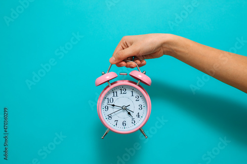 It's time to. A woman's hand holds a pink alarm clock against a blue background