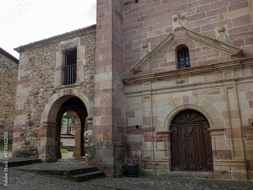 Vista de la fachade de una iglesia antigua de piedra con arcos y un campanario en el pueblo de Carmona, en la Cantabria rural de España, verano de 2020 photo