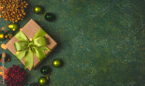 Christmas gift box with green ribbon and green christmas balls on the green stone background