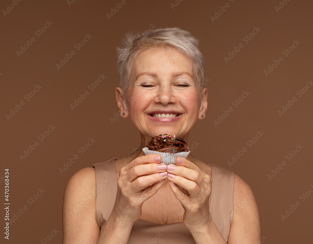 Charming elderly woman with short hair holds a chocolate cupcake in her hands. Charming elderly woman with short hair holds a chocolate cupcake in her hands.
