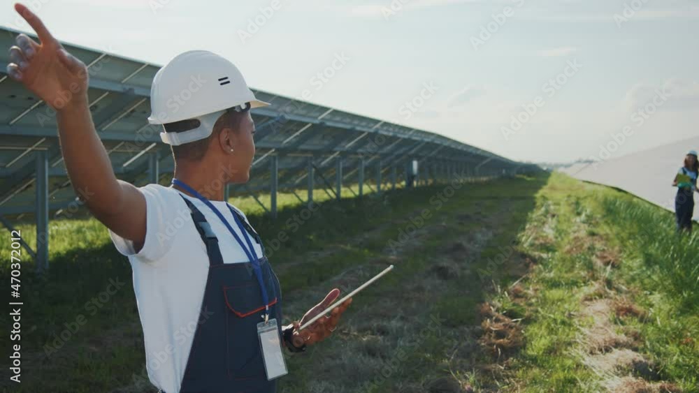 Couple of smart attractive female young engineers collaborating at modern large photovoltaic field solar station. Multi-ethnic team. Ecology workers.