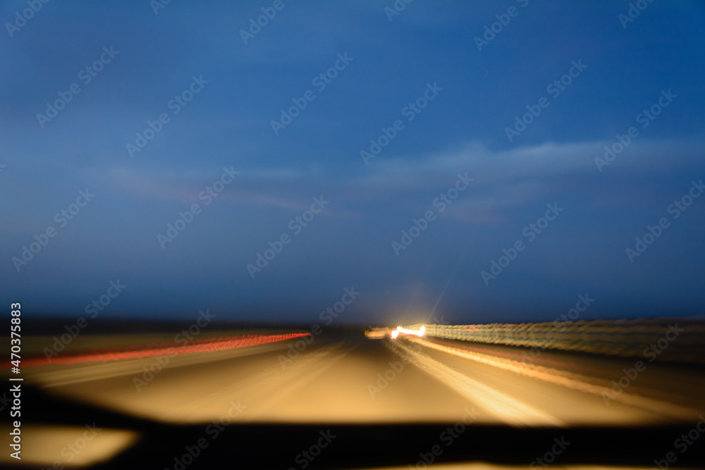 Long exposure on road with speed of light inside the car at sunset with cloudy sky. Light from the road and cars in front of the windshield wiper. blue temperature with orange, red, white light.
